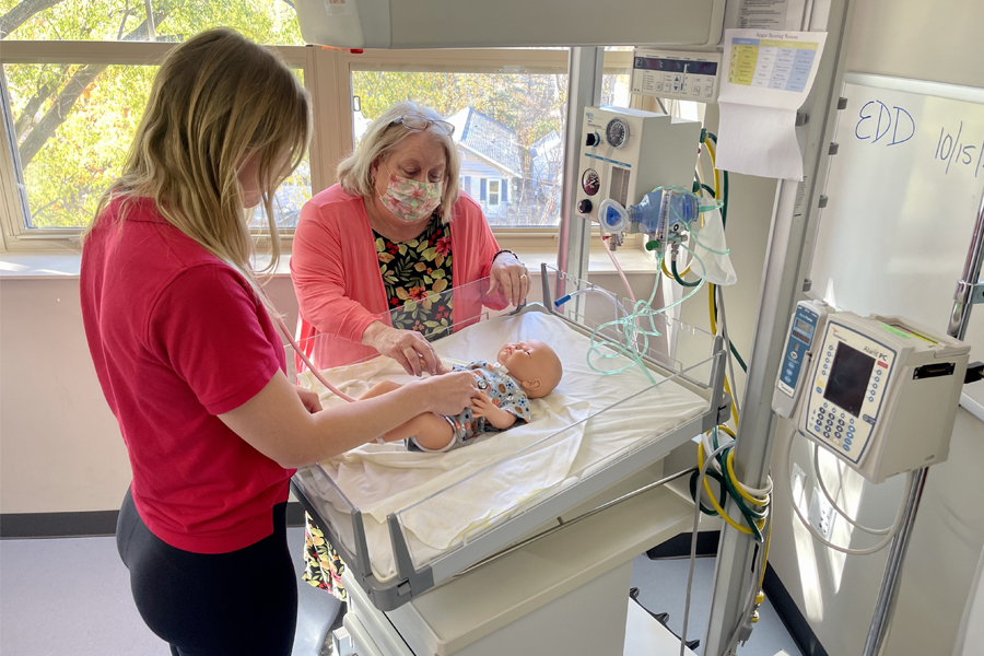 A student works with a faculty member in a simulated nursery with a baby doll.