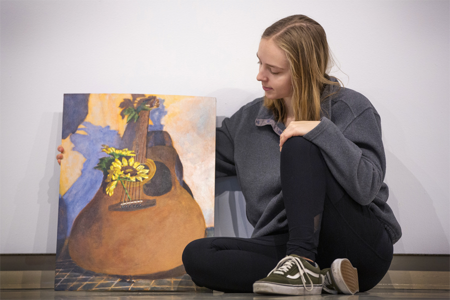 Emma Siskoff sits next to a painting of a guitar.
