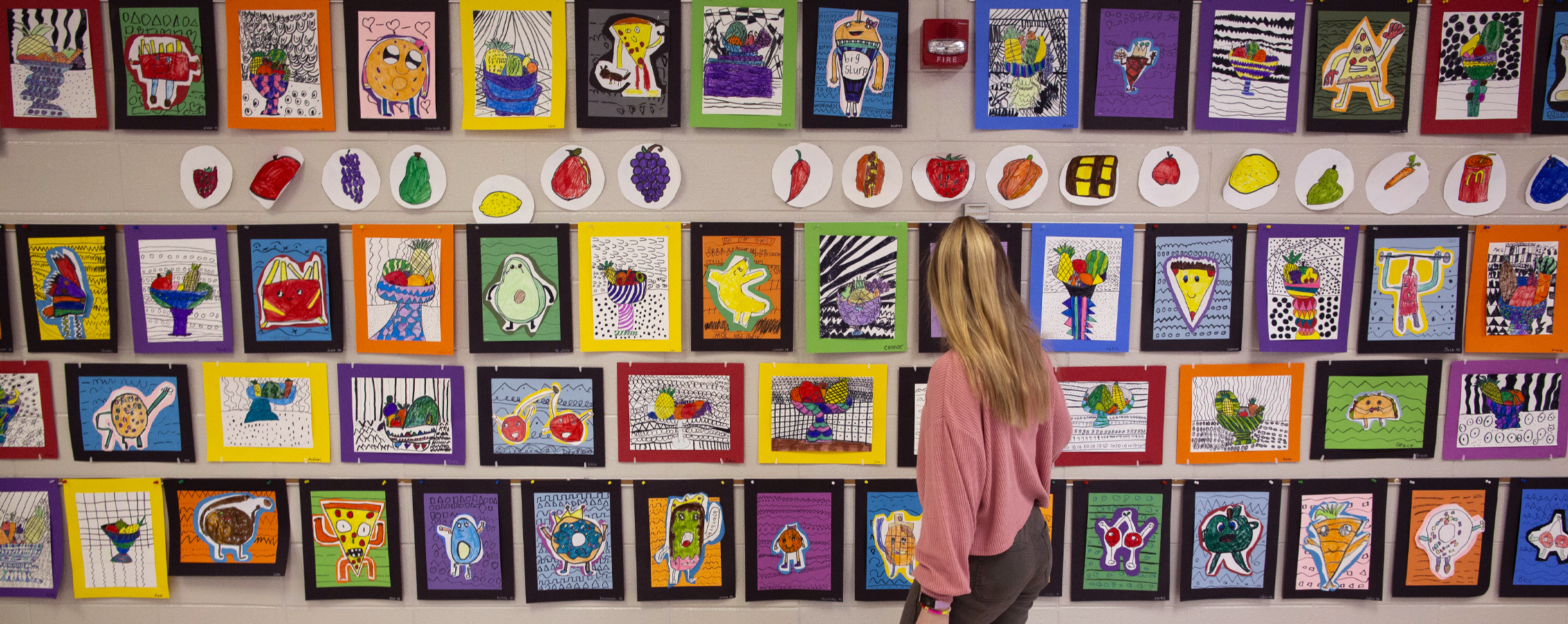 Hollyn Peterson stands in front a wall covered with colorful paintings.