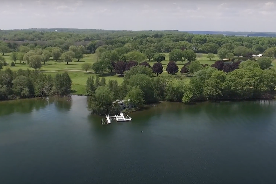 A drone shot shows the edge of a river where it connects with a wooded area.