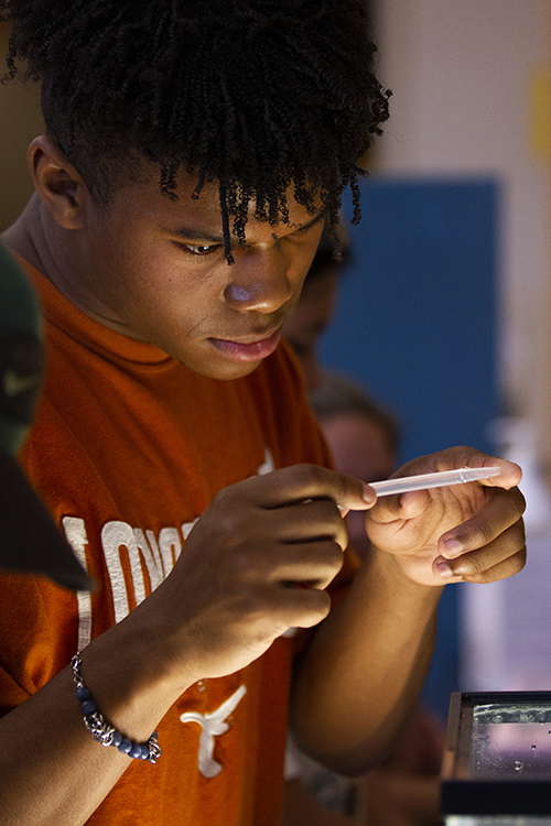 A student looks at pinpoint-sized water fleas in a vial.