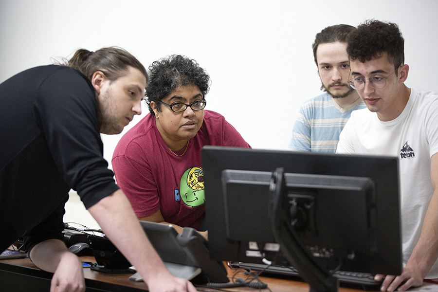 A faculty member looks at a computer with their students.