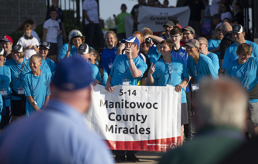 People in blue shirts hold a banner that says Manitowoc County Miracles.