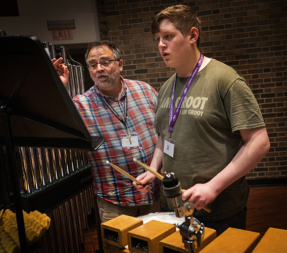 A faculty member works with a camper playing durms.
