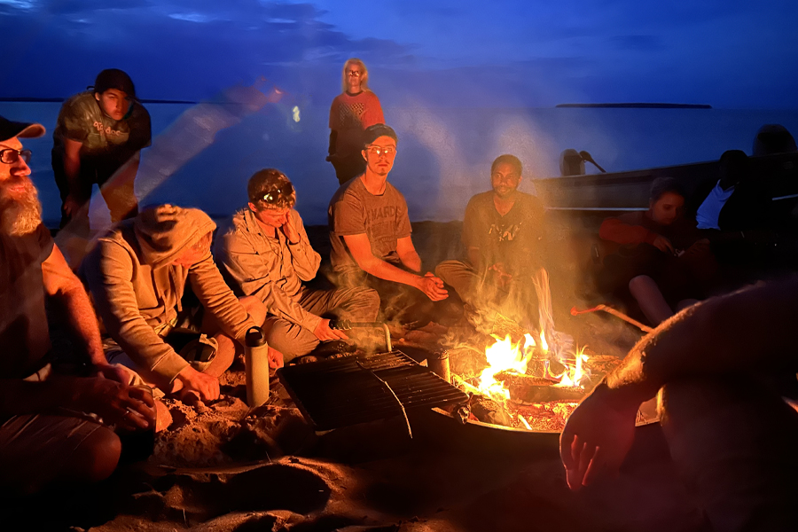 Students sit around a campfire.