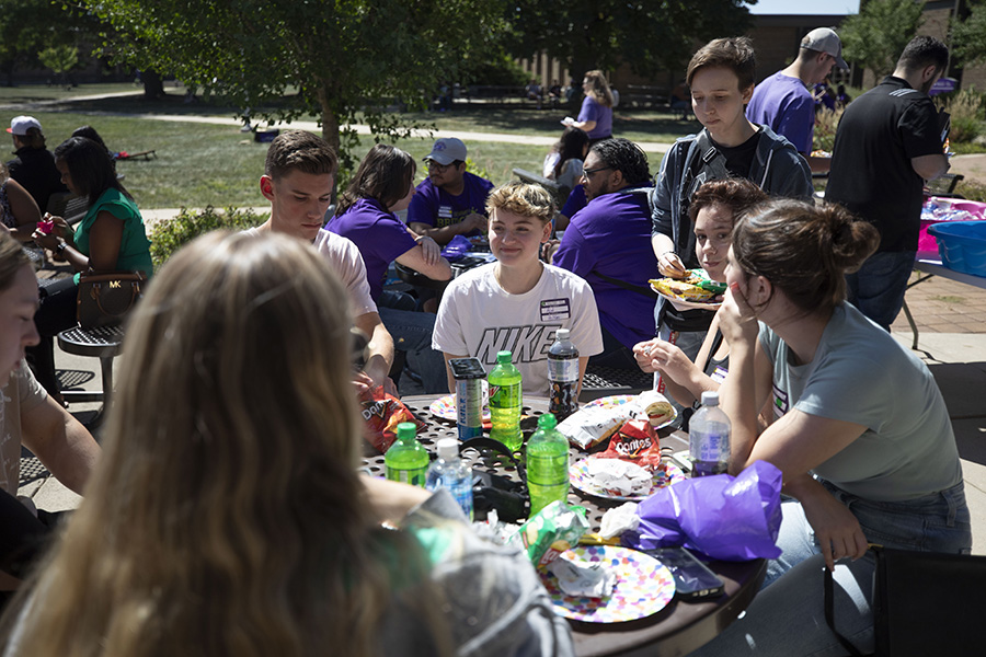 Students sit at a table outside and eat lunch together.