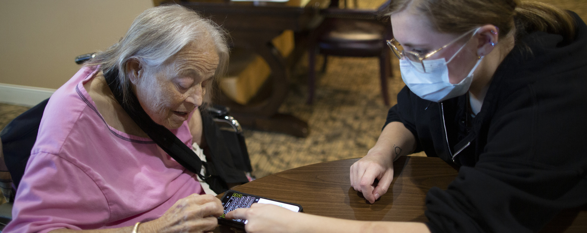 A student and a senior citizen look at a phone together.