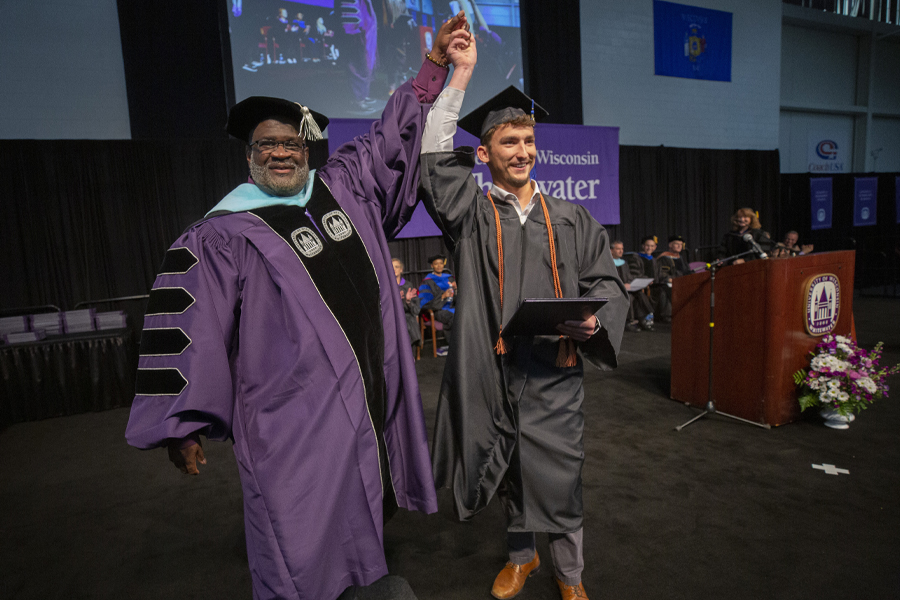 Chancellor King raises his hand with another student as they cross the stage during graduation.