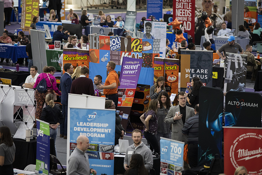 A panoramic photo of the career fair in the Fieldhouse with students and employers walking around and colorful signs representing the businesses.