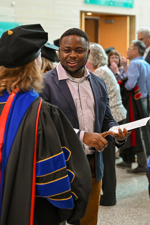 Patrice Achu speaks with a person wearing graduation Regalia.