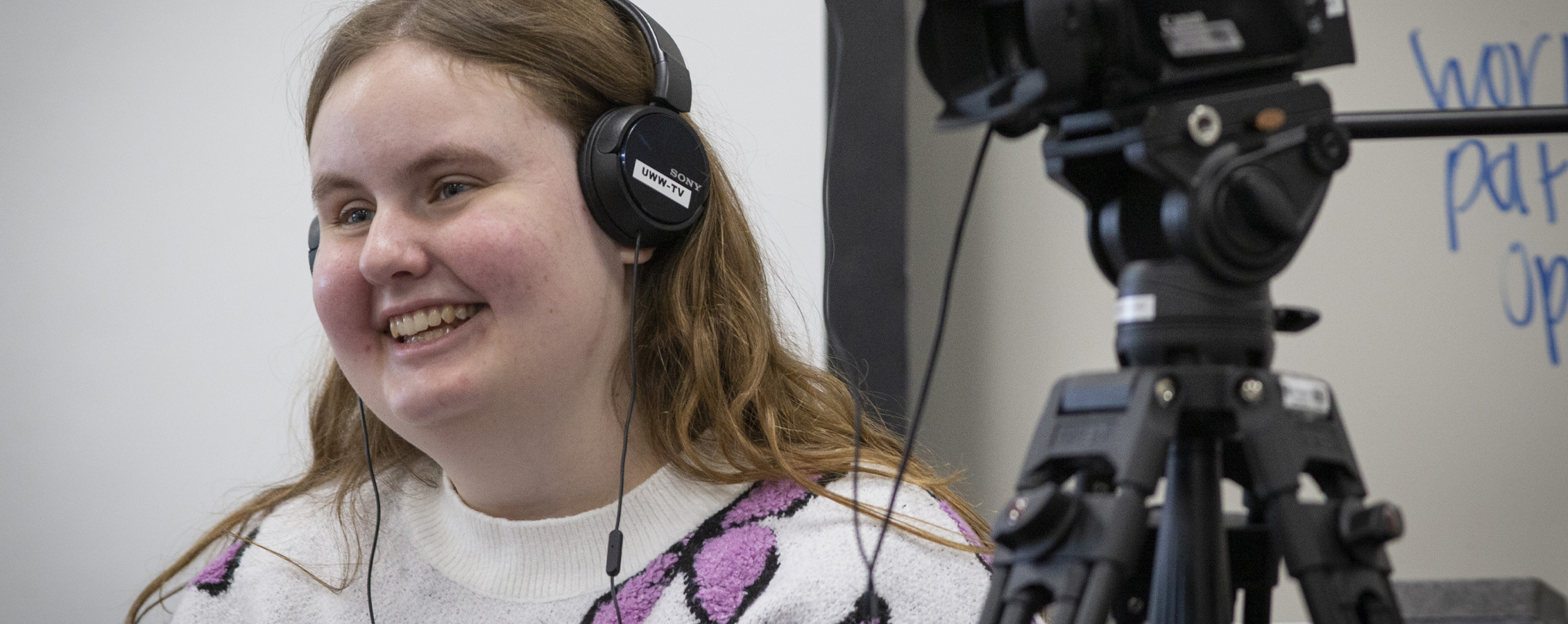 Photo of Angie Carchesi wearing headphones standing next to a video camera.