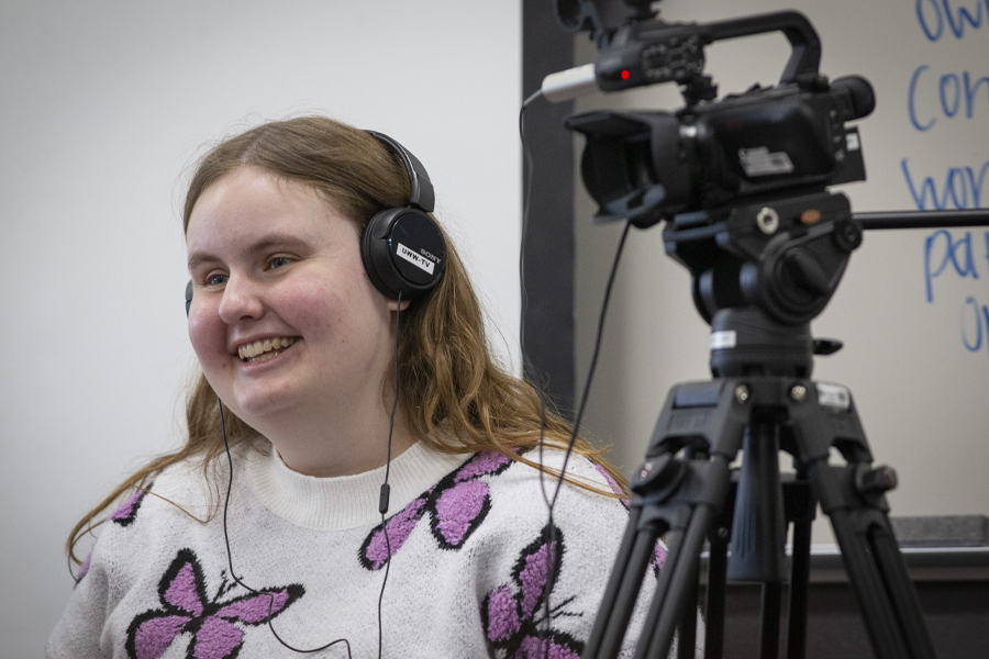 Warhawk Angie Angie Carchesi wears a headset and stands next to a video camera.