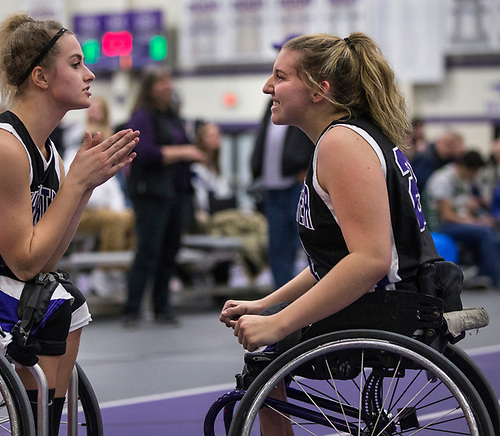Two wheelchair basketball players talk off the court.