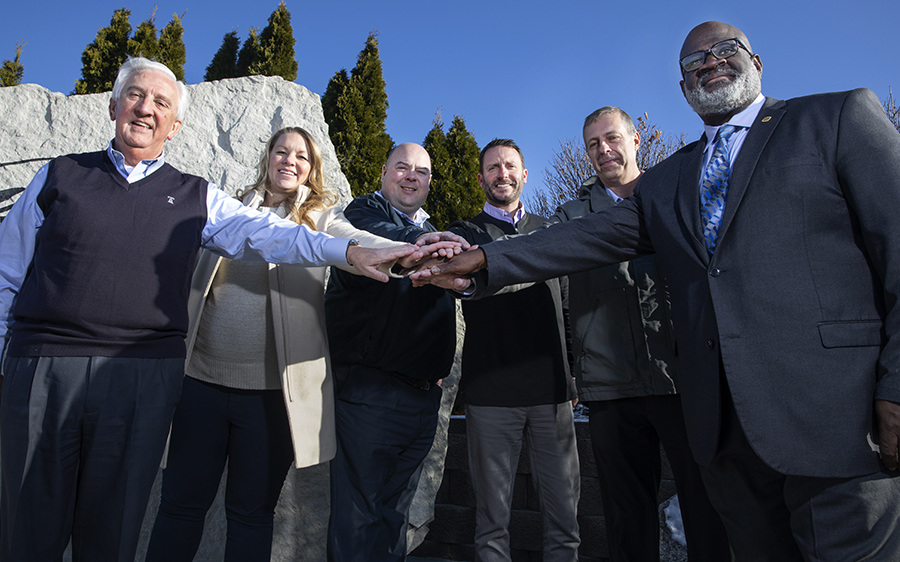 Six people stand with their hands together in a huddle.