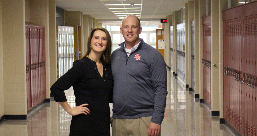 Andy Farley stands with his wife in a school hallway lined with lockers.
