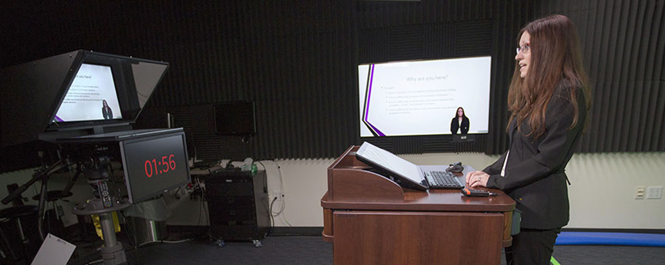 A faculty member speaks at a podium while being recorded.