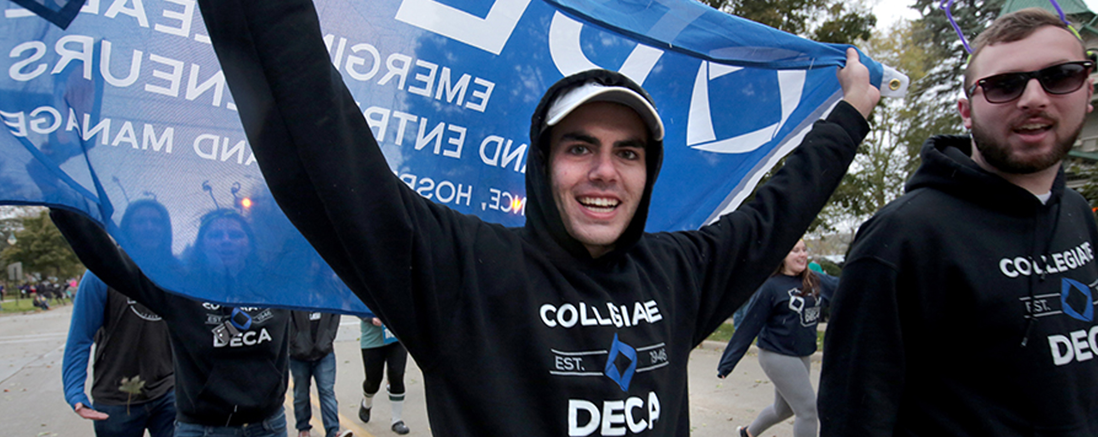 A student holds a blue DECA flag behind him while marching in the Homecoming parade.