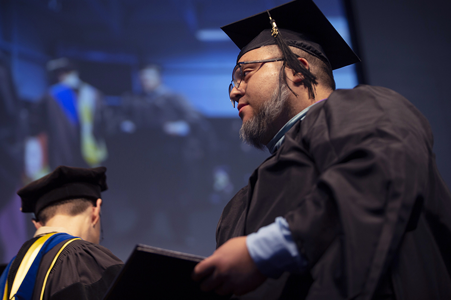 A graduate dressed in academic regalia crosses the stage.