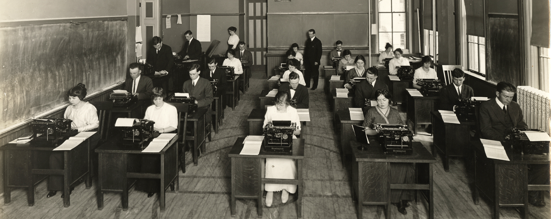 An old photo shows business students sitting at desks with typewriters in the earliest days of the business school.
