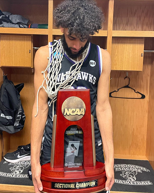 Tre Chislom wears a basketball jersey and holds a large trophy.