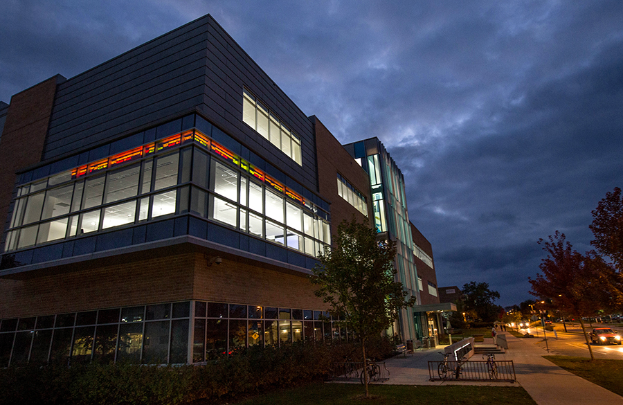 The exterior of Hyland Hall at night with the stock market ticker illuminated through the windows.