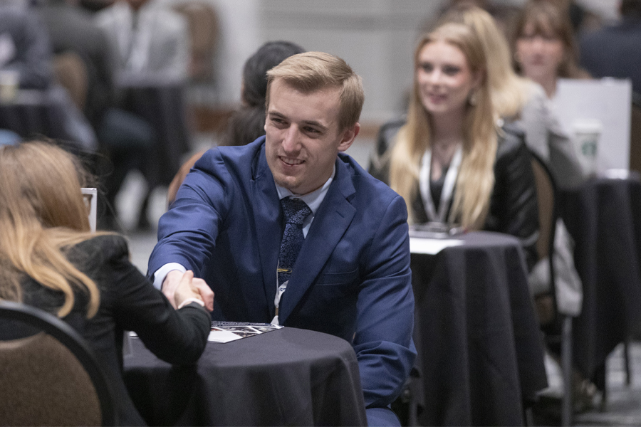 Drew Best wears a blue blazer and shakes hands with someone.