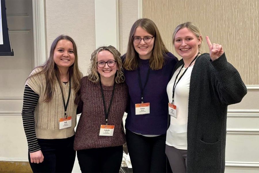 Four students link their arms together and smile for the camera.