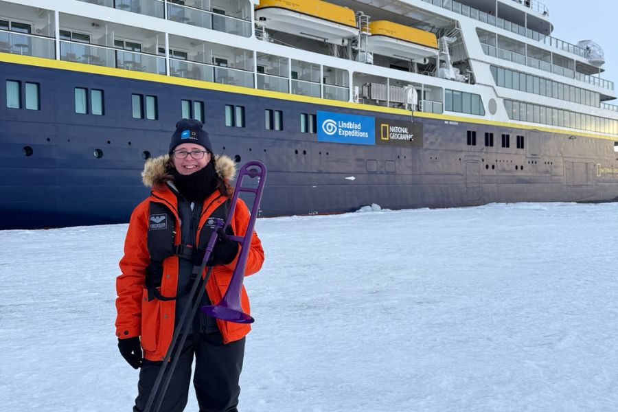 Music educator Lisa Werner with her purple trombone in front of the vessel, the Endurance, that took her to Antarctica and back.