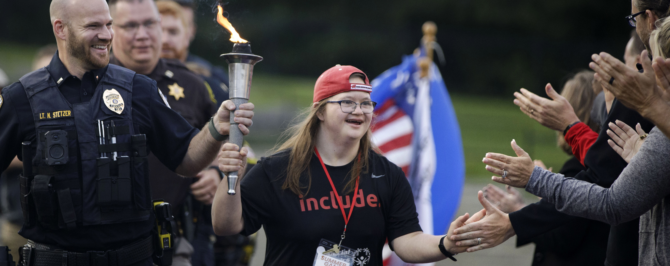 A special olympian runs through a crowd and receives high fives as they carry the ceremonial torch.