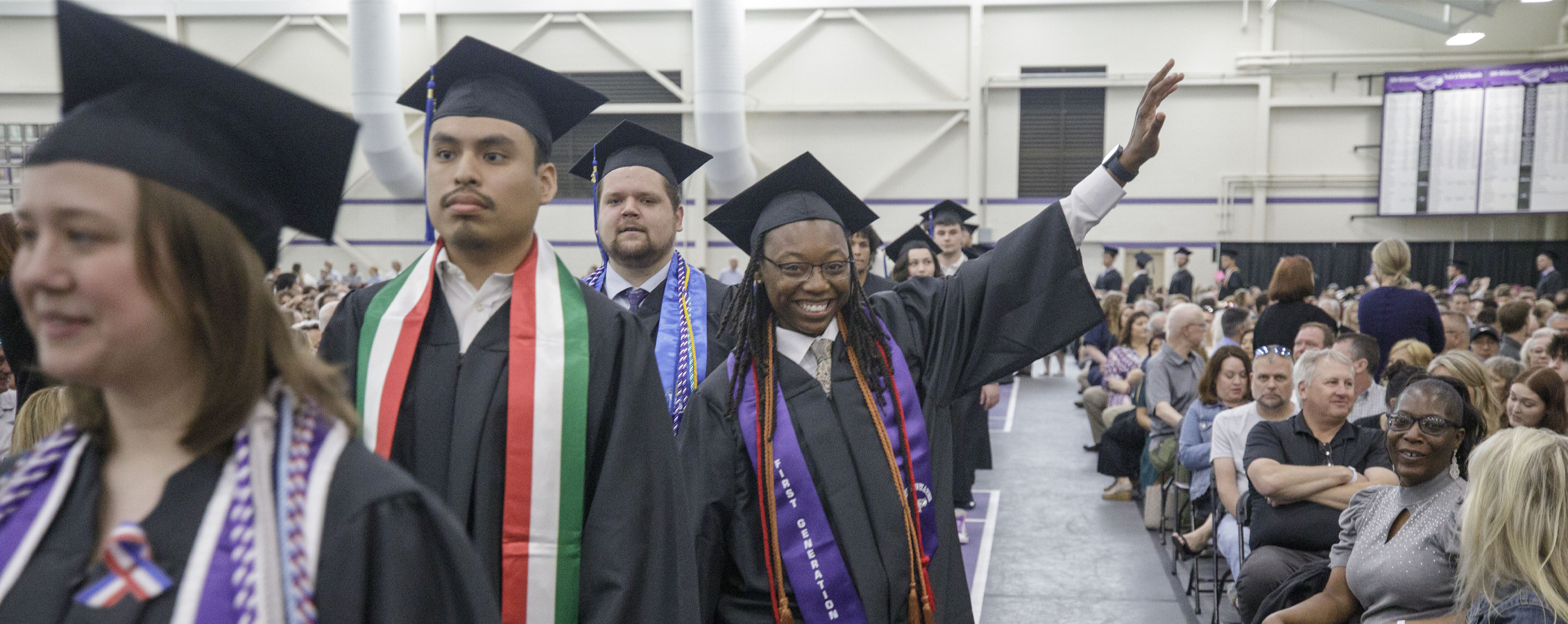 A student wearing academic regalia waves during the graduation ceremony.