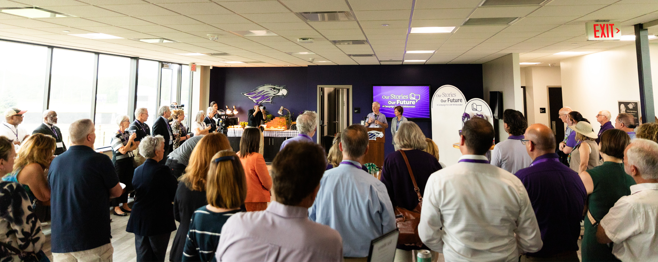 People speak at a podium in front of a large group of people.