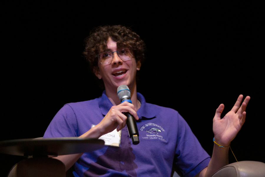 Marco speaks with a mic on hand and wearing a purple shirt.