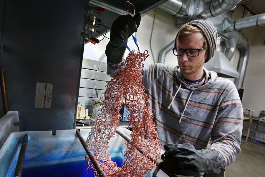 JJ Thomson working on a project as a student. A red brass necklace emerges after days in an electrically-charged acid bath, which creates different thicknesses in the metal.
