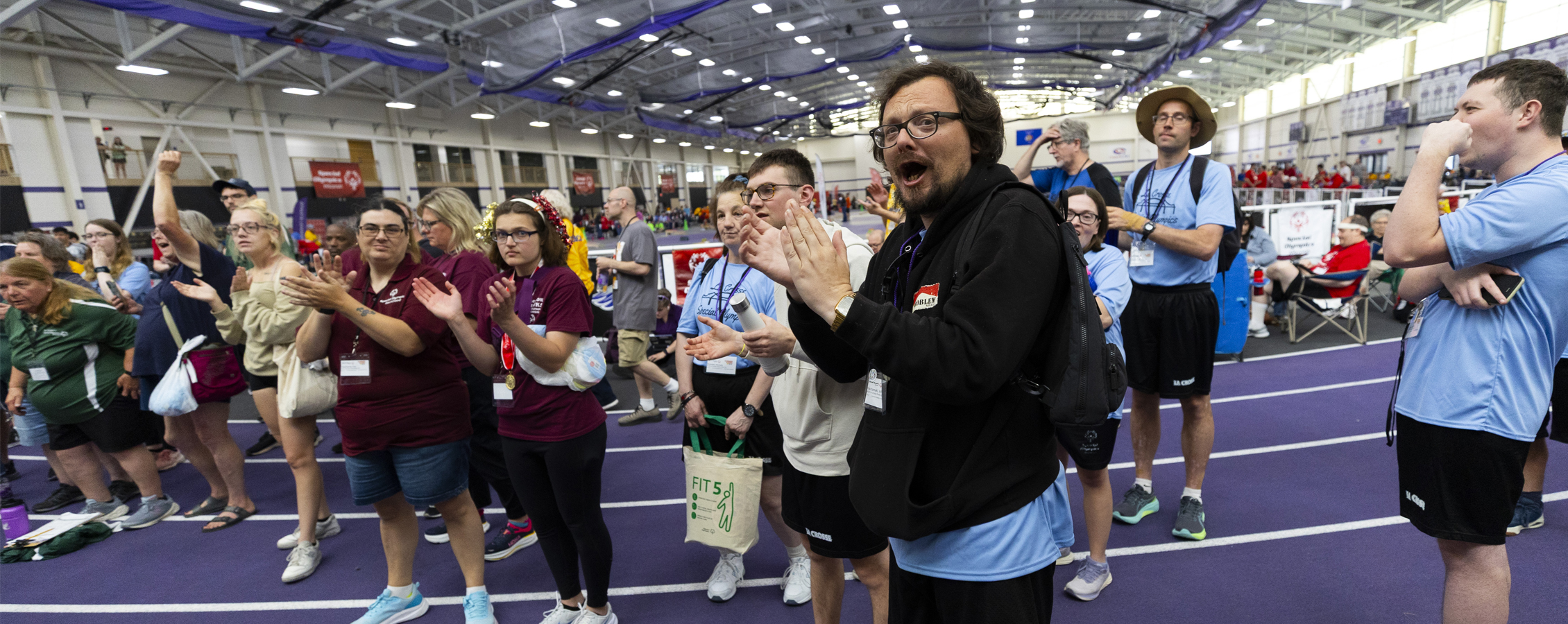 Group of people cheering in fieldhouse during Special Olympics event.