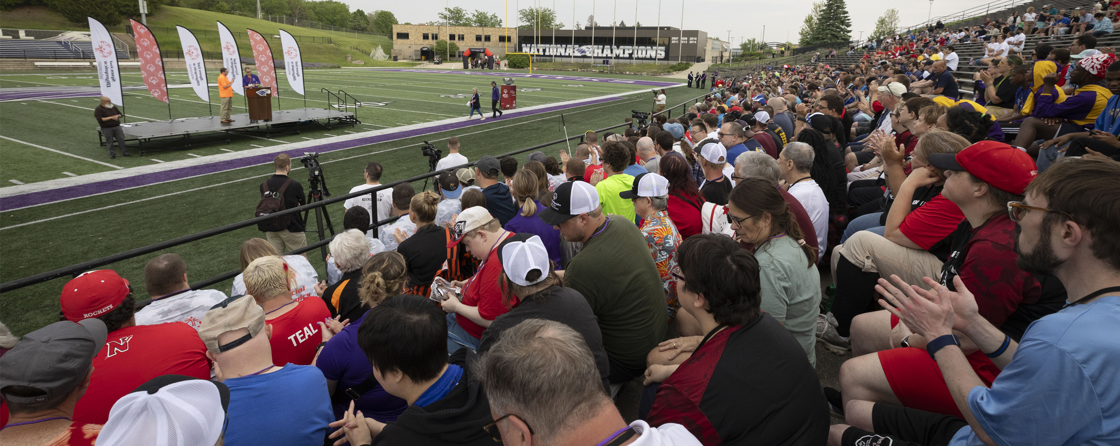 Athletes and their families watching the Special Olympics opening ceremony on football field.