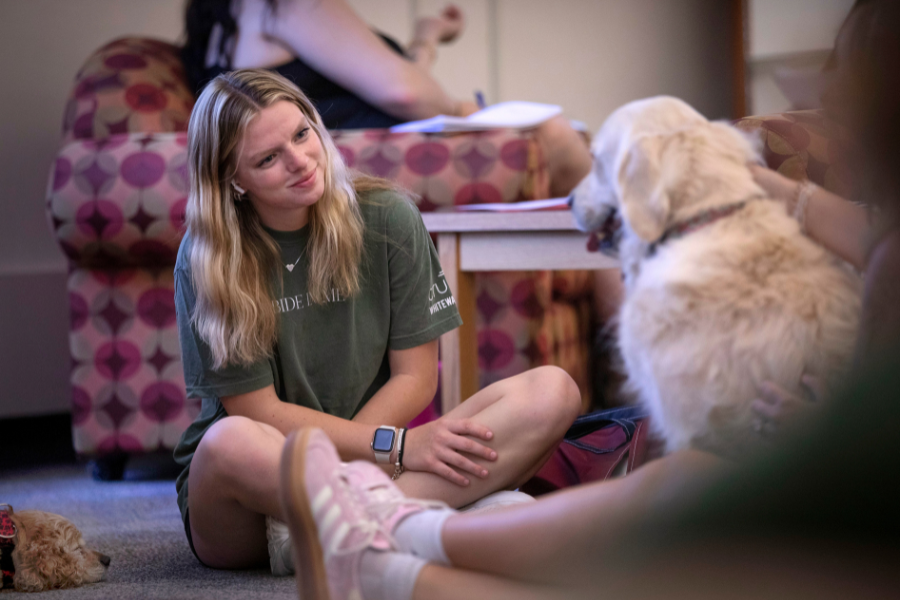 Student is at pet therapy smiling at a dog.