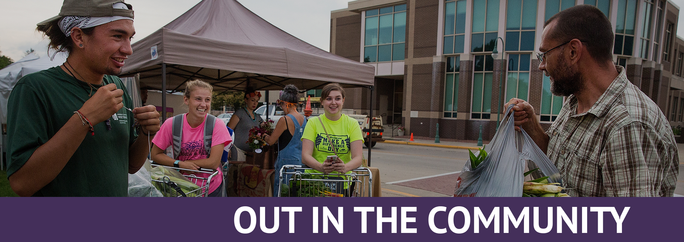 Out in the Community: Three students smiling at a market vendor handing them a bag of fresh corn