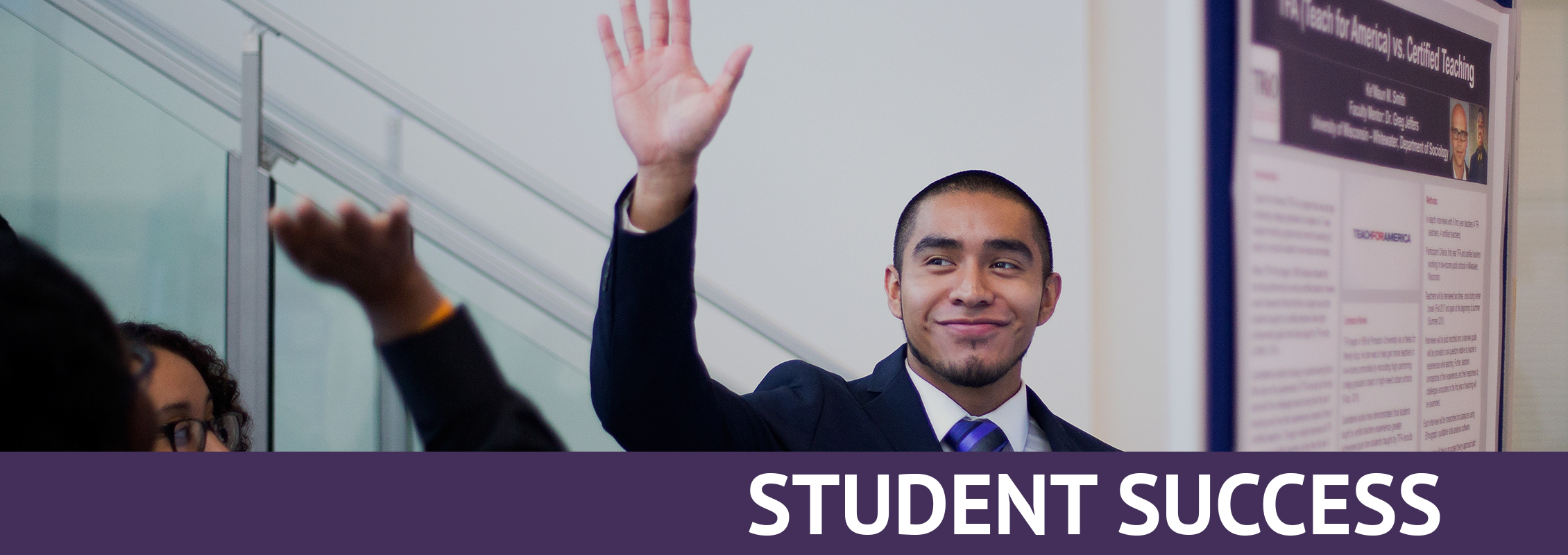 Student Success: A smiling student in a suit with his hand raised in front of his research project