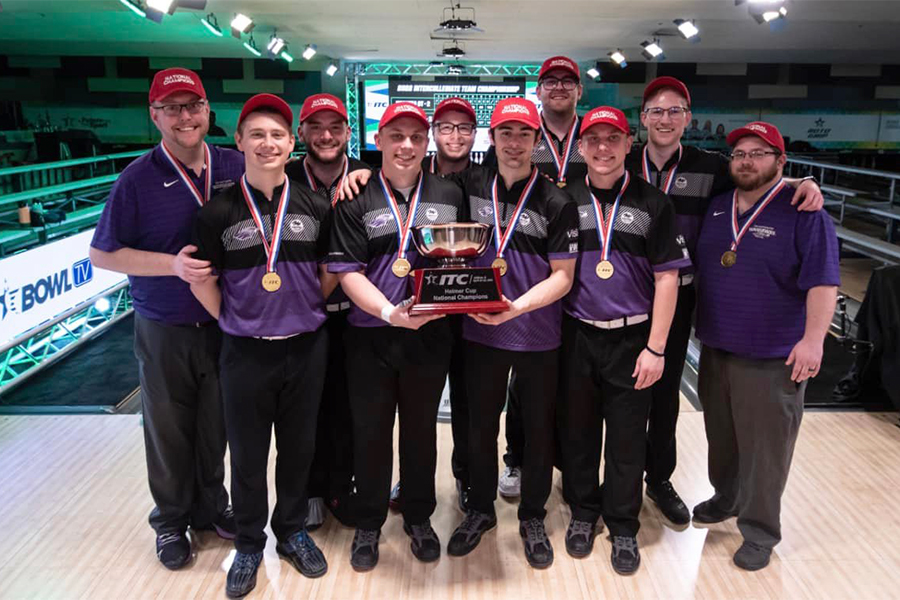 Warhawk Men's Bowling team stands in a bowling alley with their trophy.