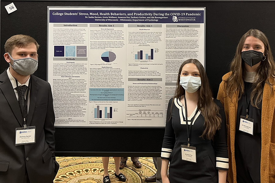 Three psychology students stand in front of their poster.