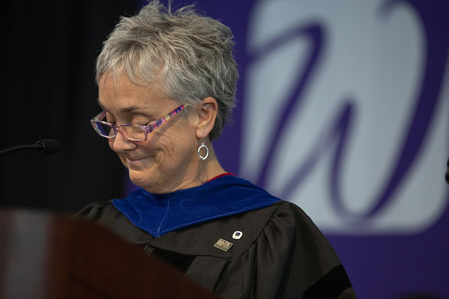 Robin Fox stands at the podium wearing a commencement robe.
