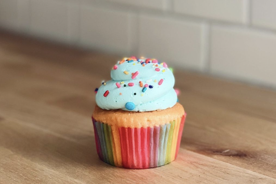 Cupcake with blue frosting and a rainbow bottom sitting on a wood counter.