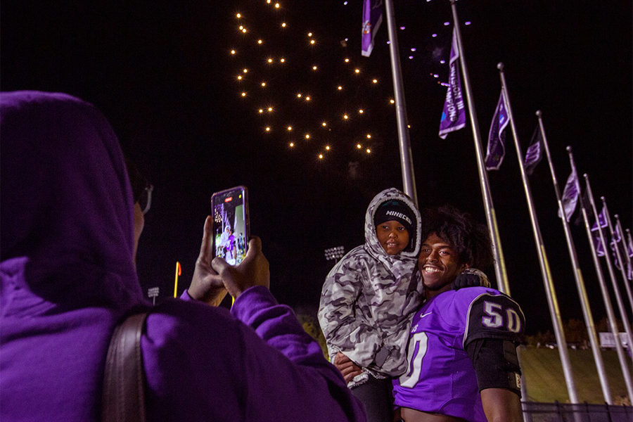 Warhawk football player takes a place with his younger brother with fireworks in the background.