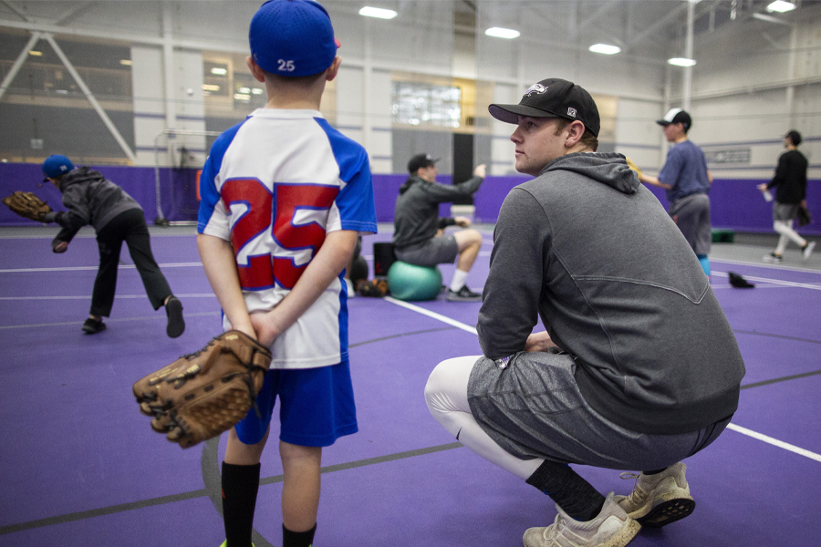 Warhawk Baseball player kneels next to a young person with a baseball glove on one hand.