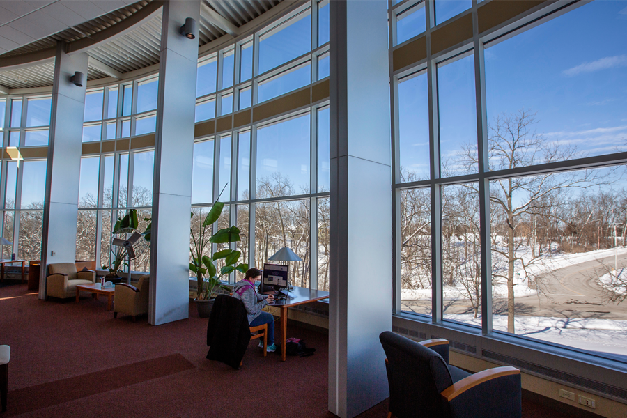 A student reads in the library in front of large windows.