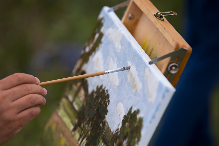 A paintbrush lays on a painting of outdoor landscape.