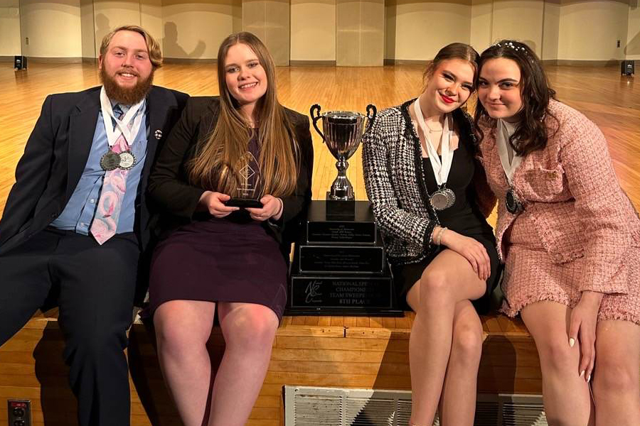 Four students sitting next to a trophy.