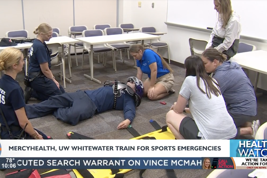 People kneel on the floor around a person wearing a football helment.