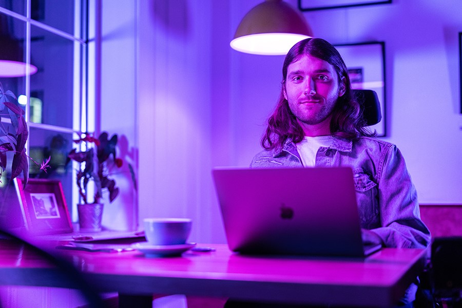 A person looks at the camera from behind a laptop.