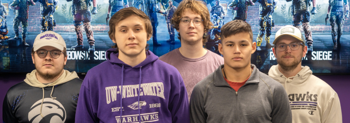 Members of the Rainbow Six: Siege Varsity Esports team standing in front of a poster